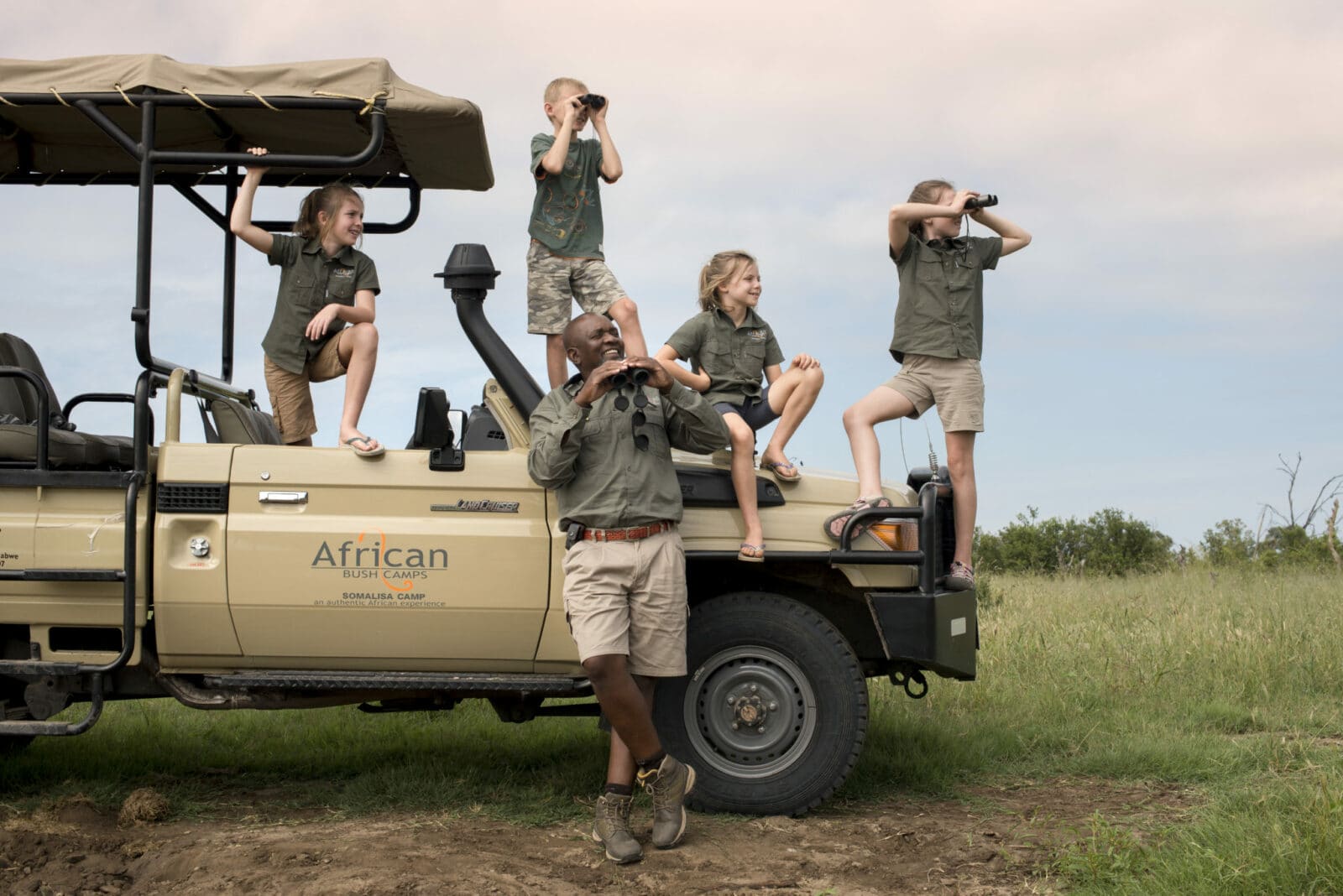 young happy children sitting or standing on a safari vehicle with their guide looking through binoculars