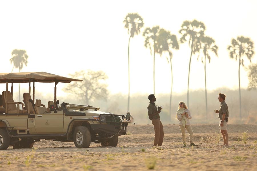 three people standing next to a safari vehicle enjoying the outdoors in Tanzania's Ruaha National Park